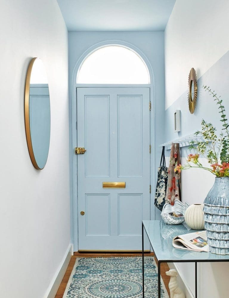 Bien aménager et décorer son entrée avec une porte d'entrée bleu ciel. Carrelage bleu et blanc. Miroir doré et console en métal.