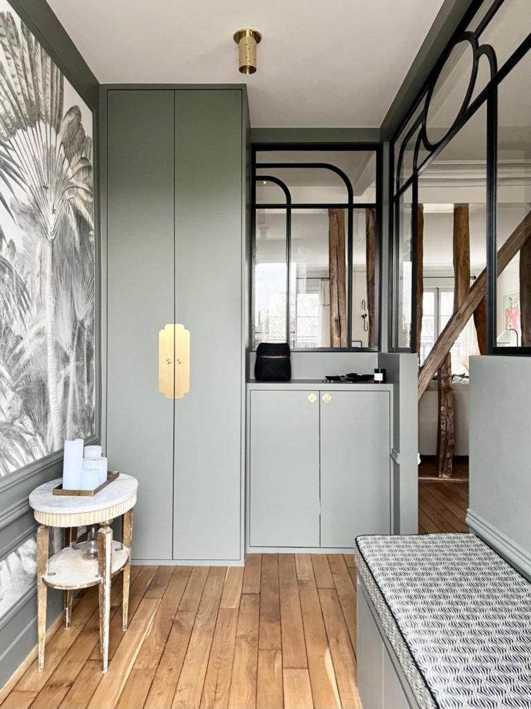 Bien aménager son entrée. Entrée avec verrière courbe noire. Meuble sur mesure vert sauge et doré. Banquette sur mesure. Papier peint végétale noir et blanc.